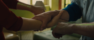 Screenshot from In Time (2011): hands clasping during a time transfer, showing the green countdown clocks on each forearm