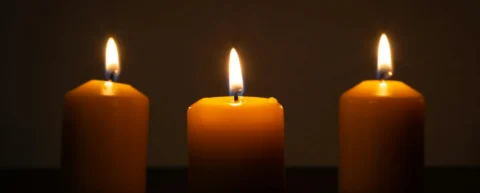 Candles lit in a dark church, casting warm light across empty pews