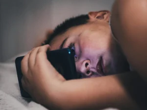 Teenager illuminated by smartphone screen glow at night, representing social media use among youth