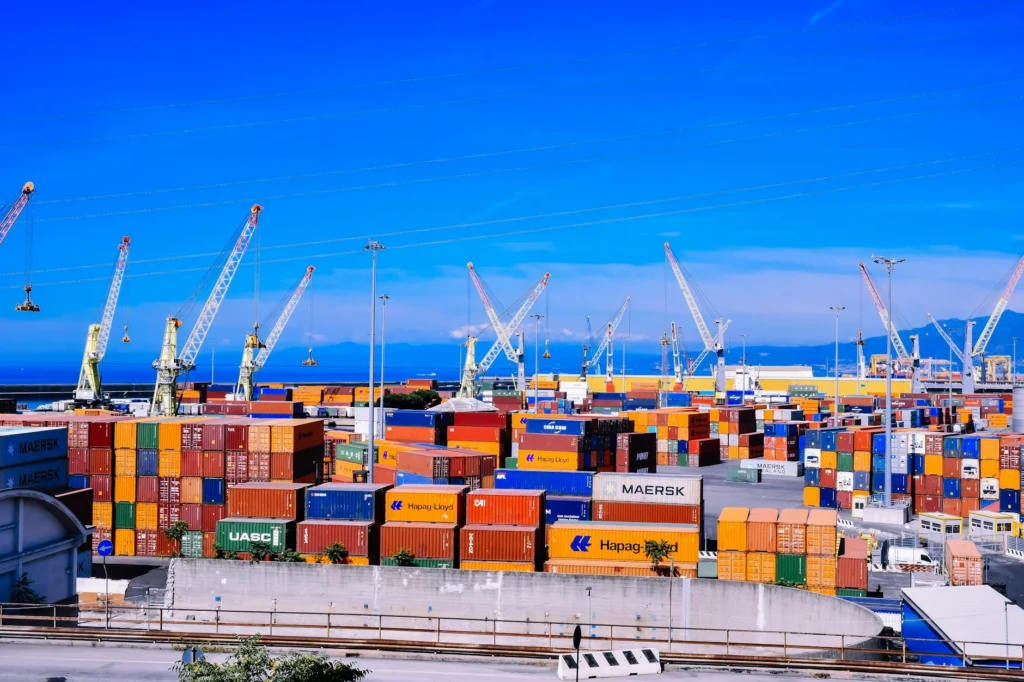 Stacked cargo containers at shipping port illustrating tariff war collapse risk to global logistics