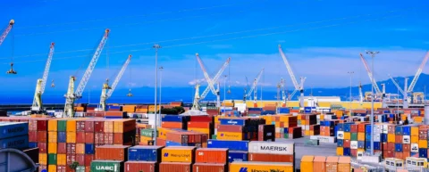 Stacked cargo containers at shipping port illustrating tariff war collapse risk to global logistics