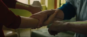 Screenshot from In Time (2011): hands clasping during a time transfer, showing the green countdown clocks on each forearm