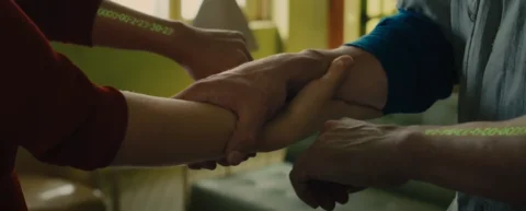 Screenshot from In Time (2011): hands clasping during a time transfer, showing the green countdown clocks on each forearm